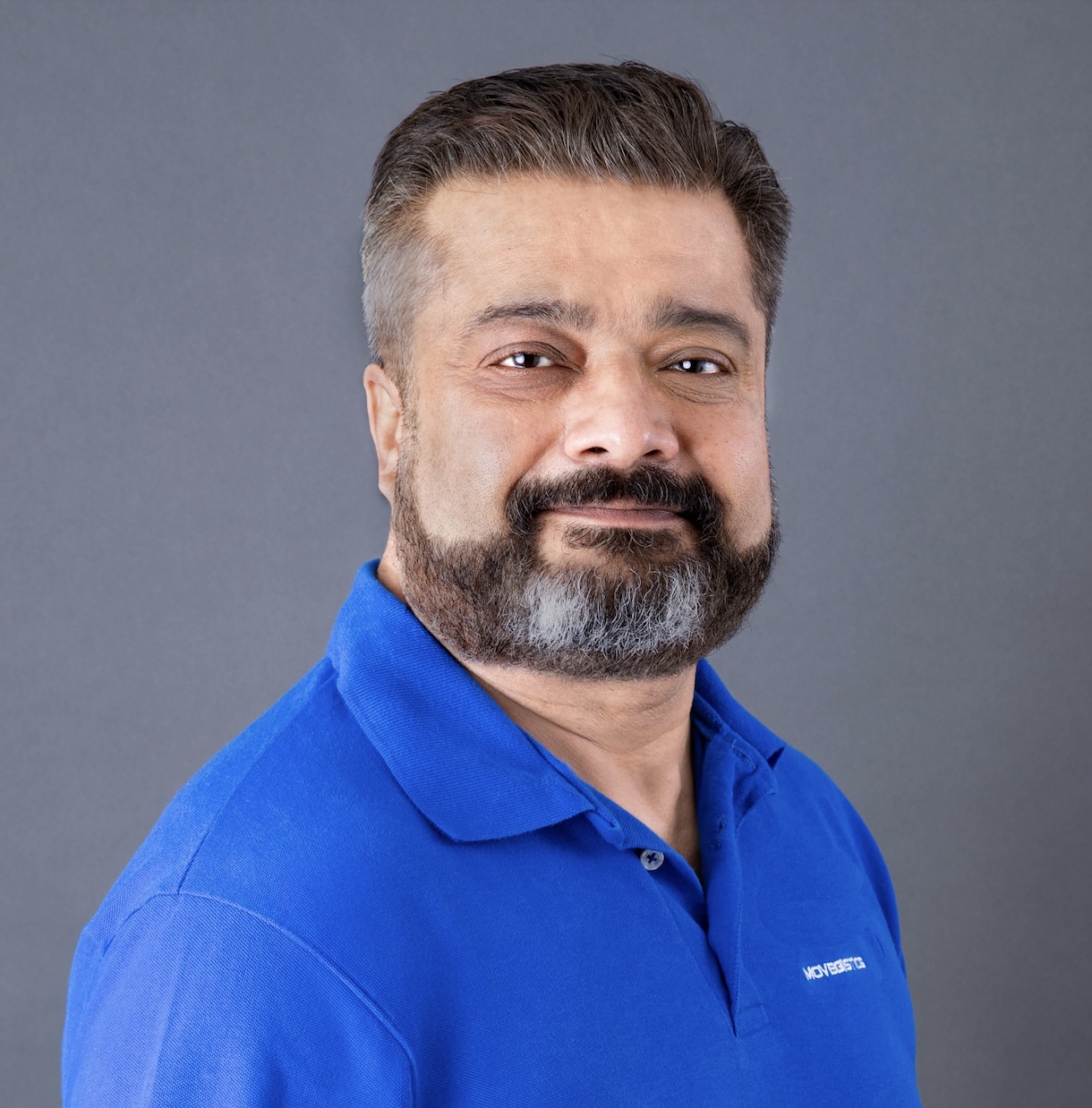 Portrait of Adarsh Dattani, Founder & CEO of Netensity Corp., wearing a blue Movegistics polo shirt, alongside a message highlighting Movegistics’ transformation of the moving industry over 15 years, the launch of Movegistics 5.0, and the company’s 2025 goal to introduce cutting-edge AI solutions for enhanced revenue and profitability.